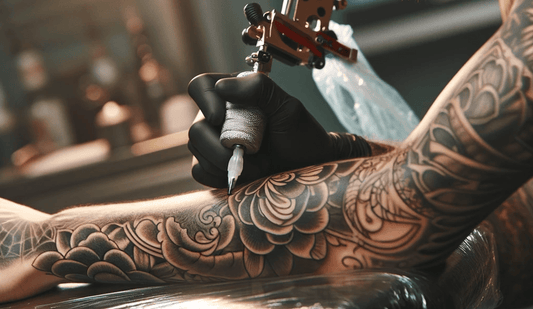 Tattoo artist working on detailed floral sleeve tattoo with tattoo machine.